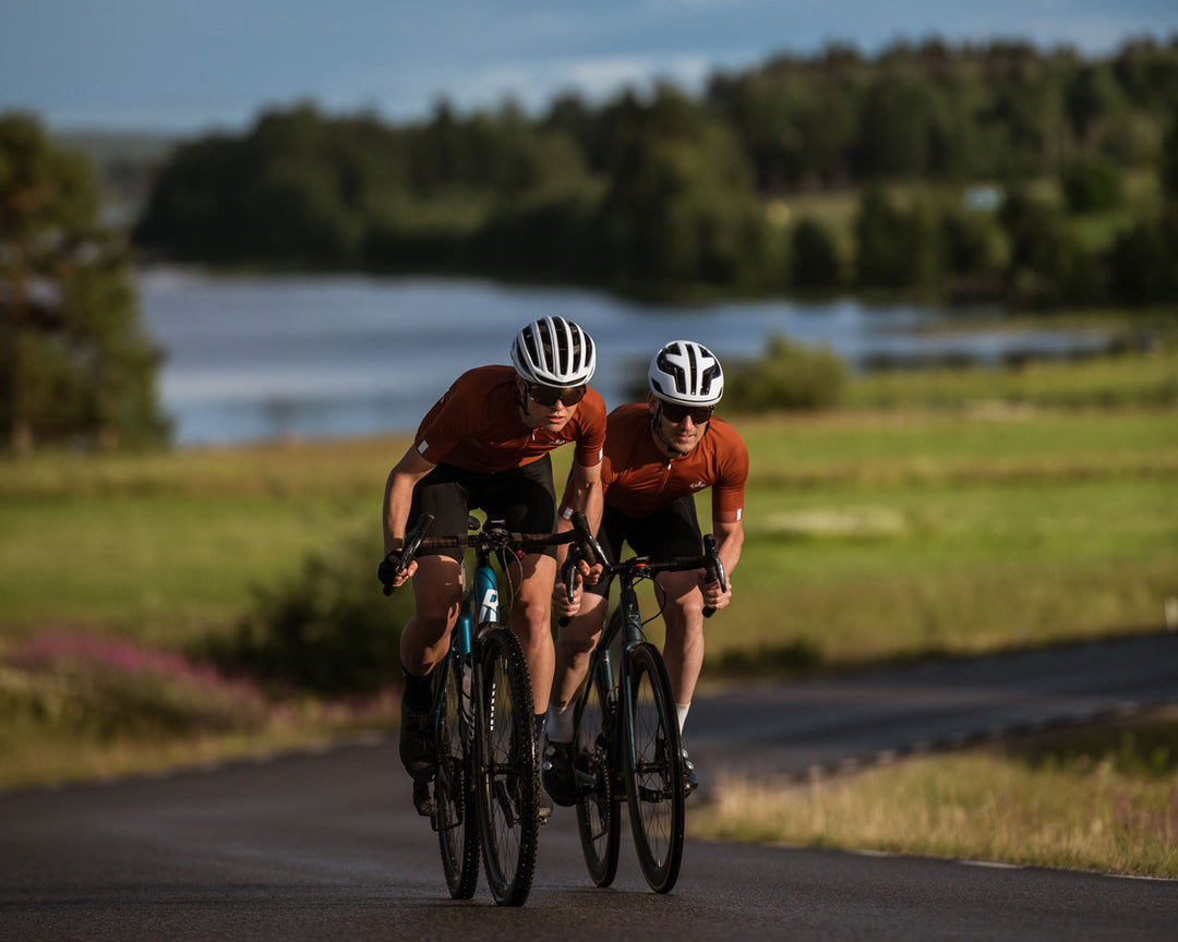 Two cyclists wearing Sigr cycling jerseys in a beautiful Swedish landscape.